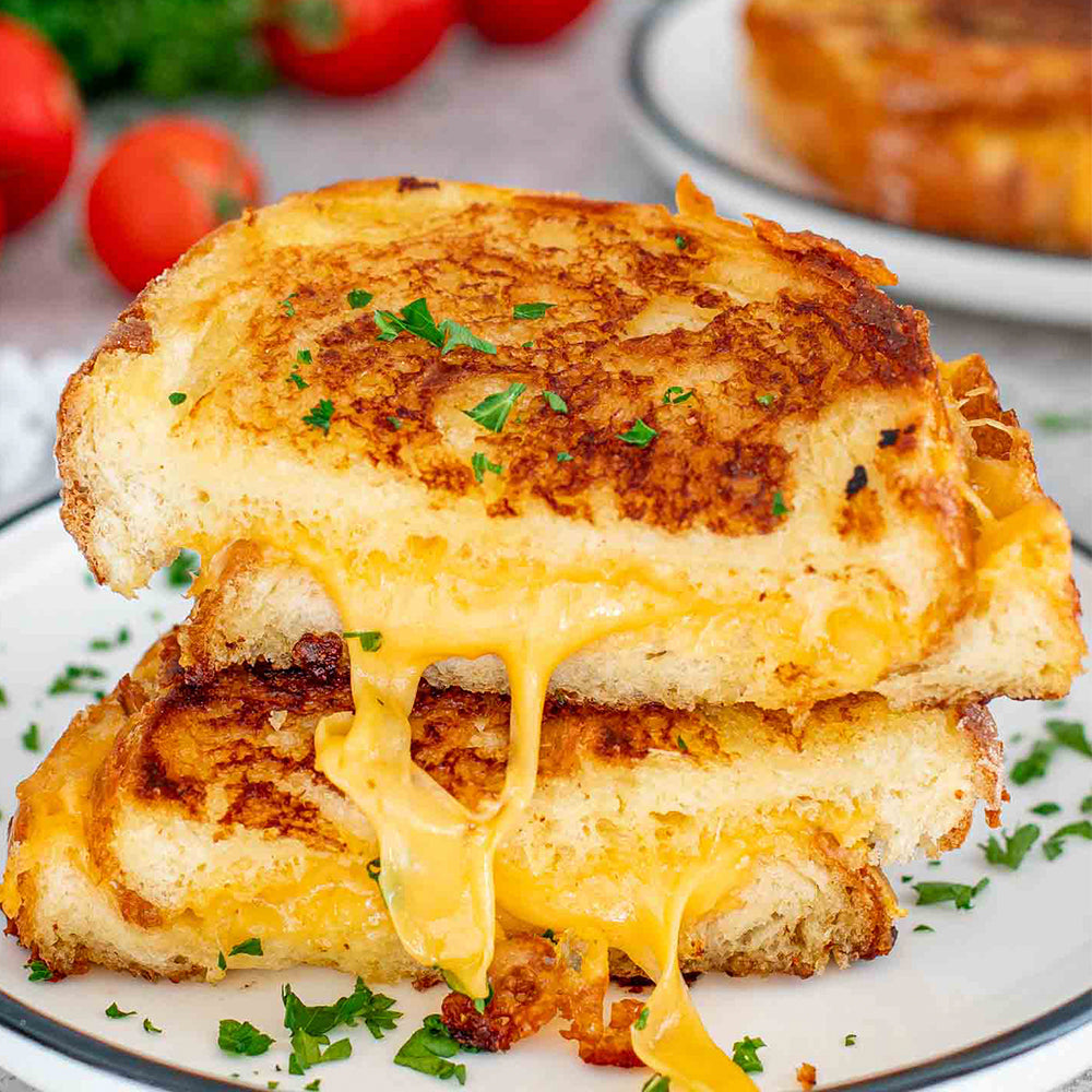 Stack of grilled cheese sandwich on a plate with tomatoes in the background