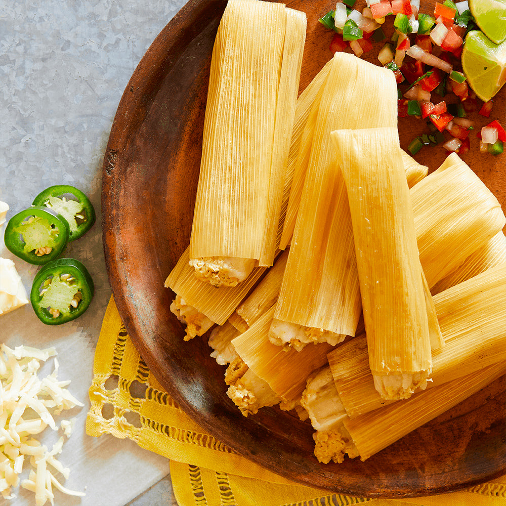 Wooden plate with tamales, jalapeños, and lime on a light background