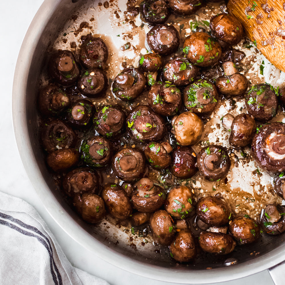 Mushrooms being sautéed in a pan with a wooden spoon