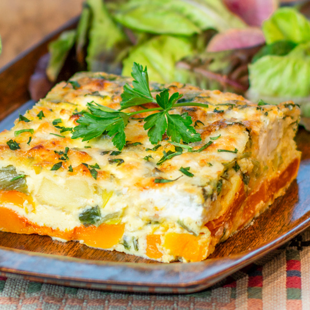 Slice of vegetable lasagna on a wooden plate with a checkered tablecloth in the background