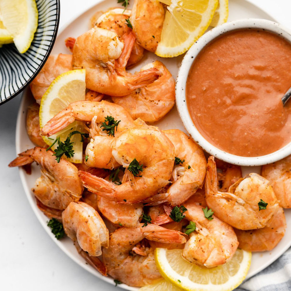 Platter of shrimp with lemon slices and a side of red sauce on a white plate.