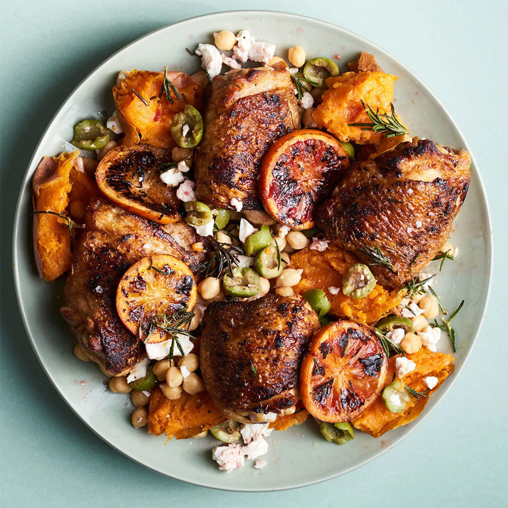 Plated dish of roasted chicken with sweet potatoes, chickpeas, and citrus on a light blue background