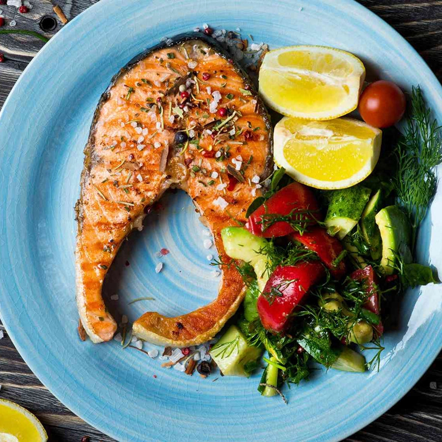 Grilled salmon with lemon wedges and a side salad on a blue plate.