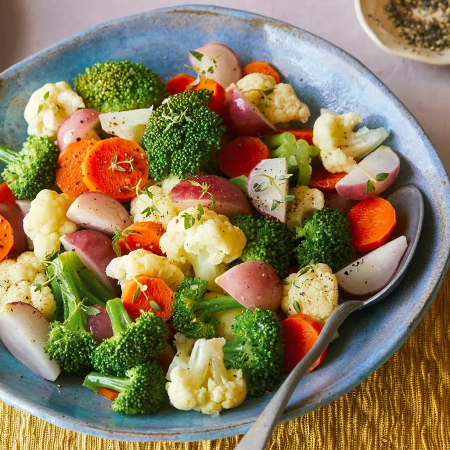 Assorted vegetables including broccoli, carrots, and cauliflower in a blue bowl with a spoon.