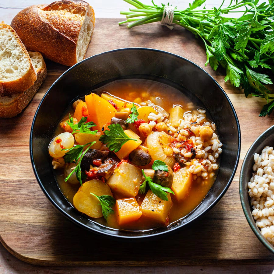 Bowl of vegetable stew with bread and herbs on a wooden board