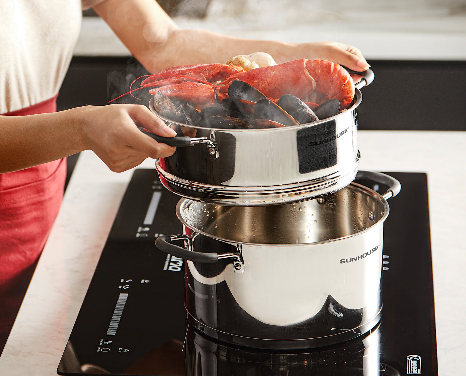 Person cooking lobsters in a double boiler on a stove