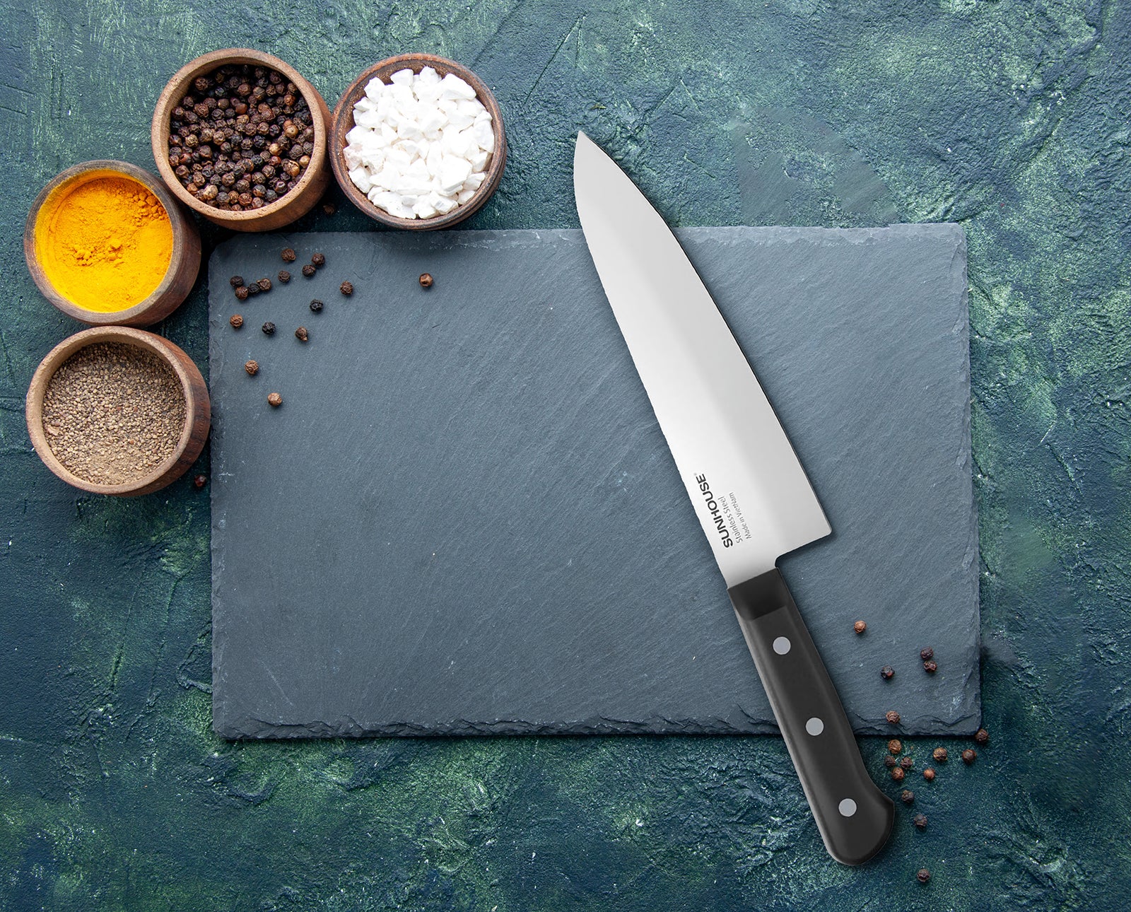 Sunhouse Knife on a slate surface with bowls of spices on a textured blue background