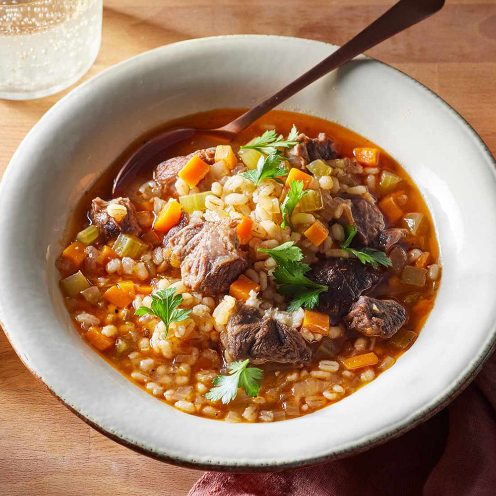 Bowl of beef and barley soup with vegetables on a wooden table