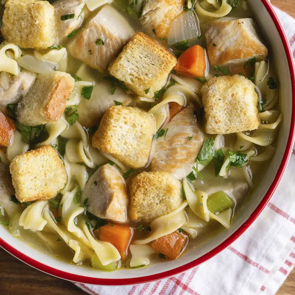 Bowl of chicken noodle soup with croutons on a wooden table