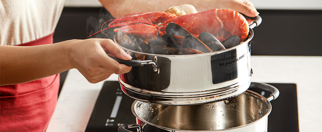 Person holding a Sunhouse steamer basket with lobsters over a pot on a stove.