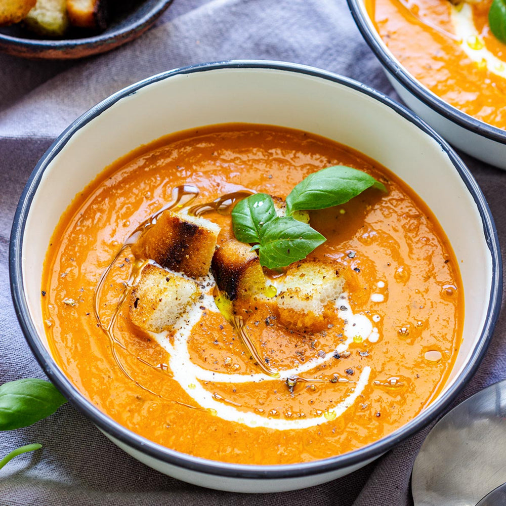 Bowl of tomato soup with croutons and basil leaves on a textured surface