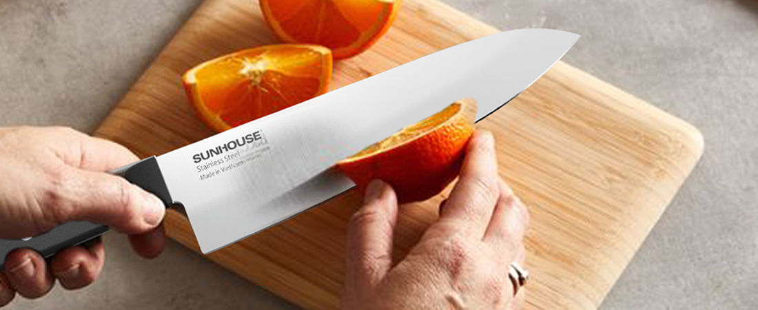 Person using a Sunhouse knife to cut an orange on a wooden cutting board.