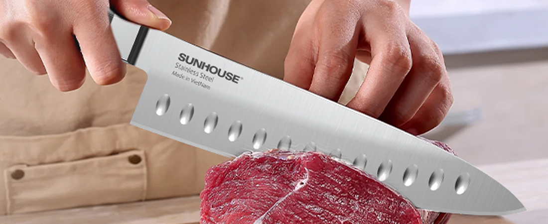 Sunhouse knife being used to cut meat on a wooden cutting board.