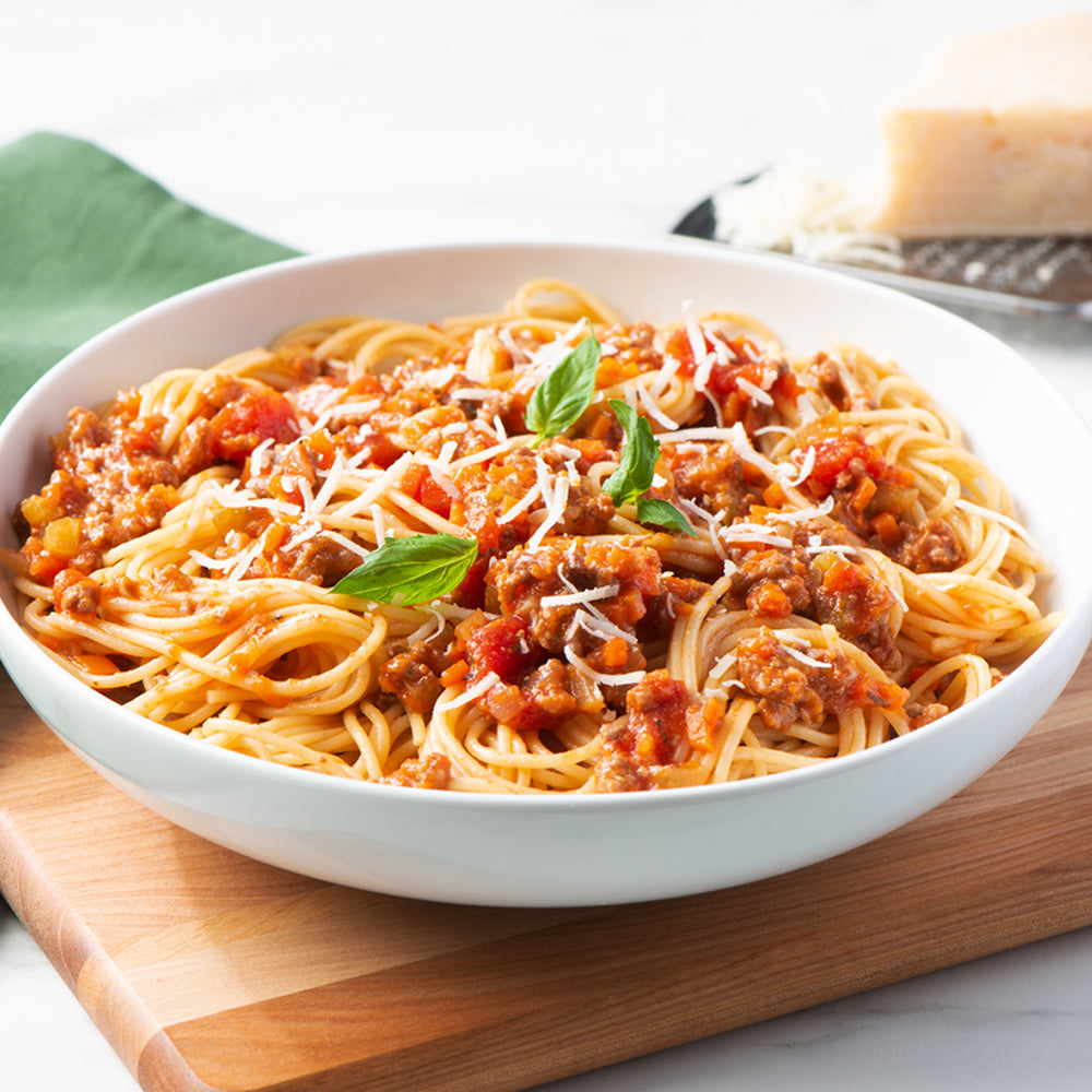 Bowl of spaghetti with tomato sauce and basil on a wooden cutting board.