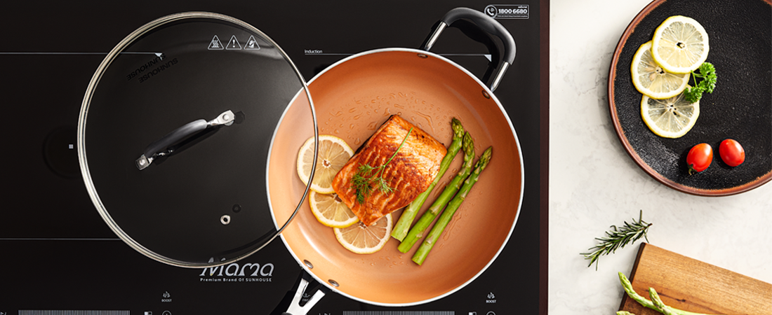 Cooking Sunhouse pan with lid, salmon dish, and lemon slices on a kitchen counter.